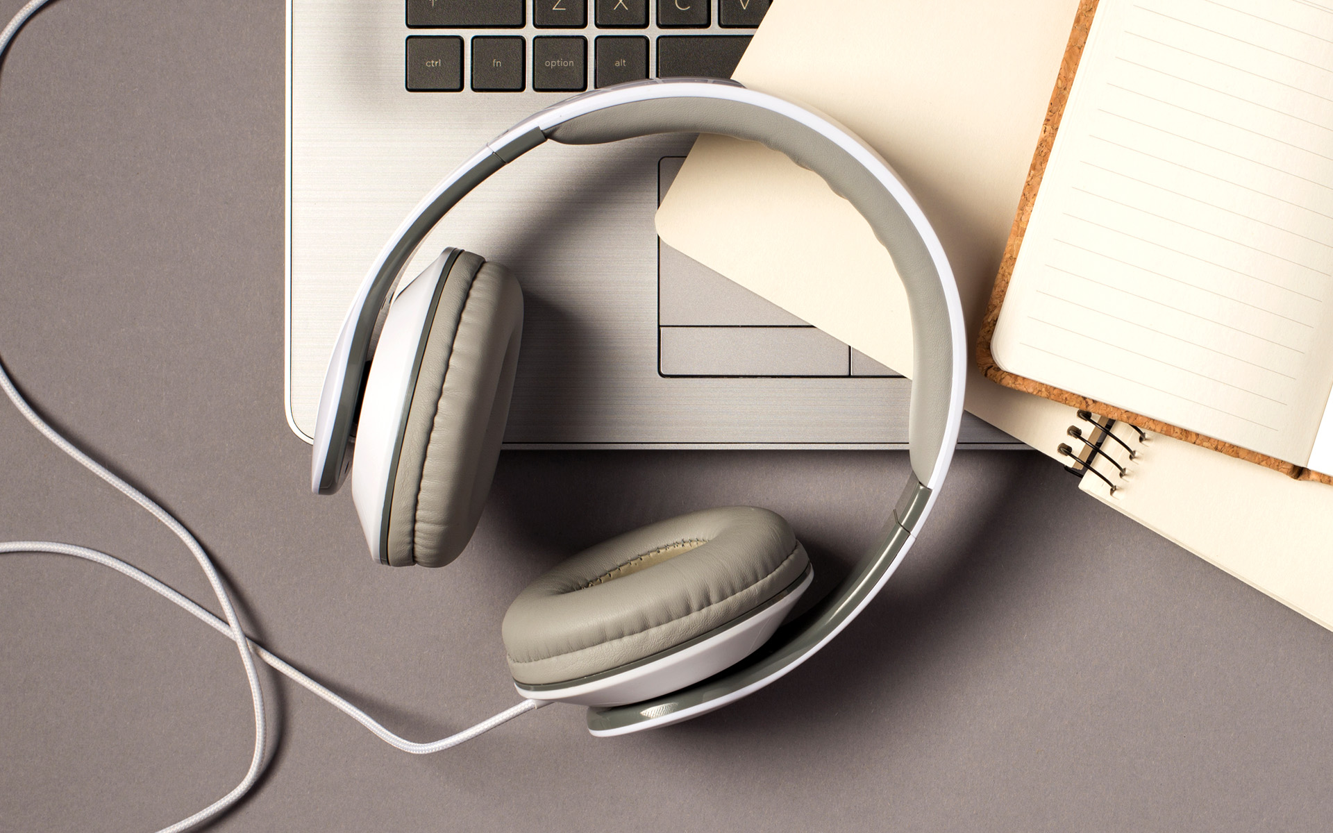 A laptop with a headphone set and notebooks lying on top of the keyboard