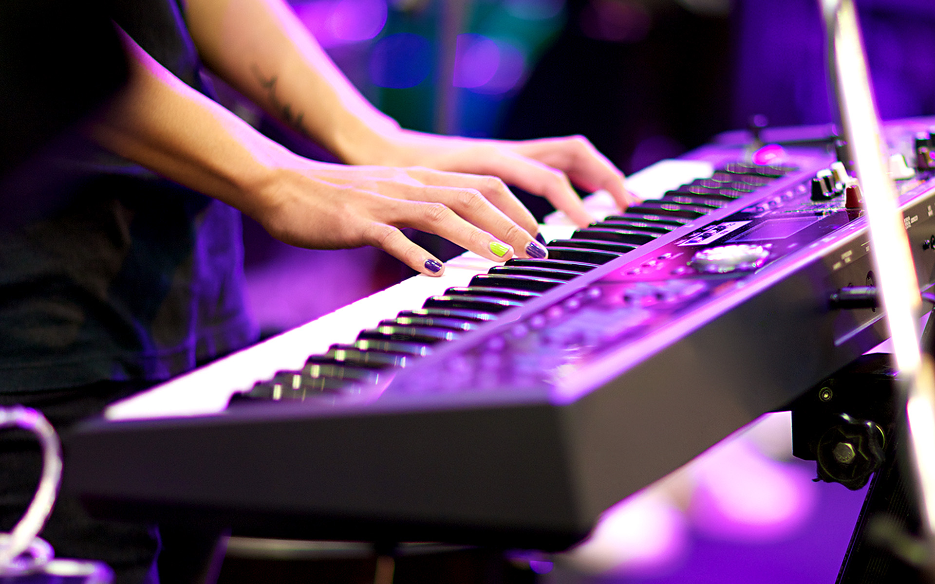 A musician with colorful nail polish on their fingernails plays a professional keyboard rig in a live concert.